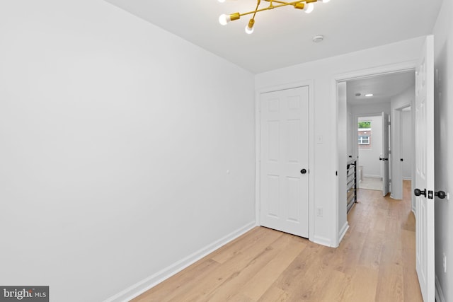unfurnished bedroom with light wood finished floors, baseboards, and a chandelier