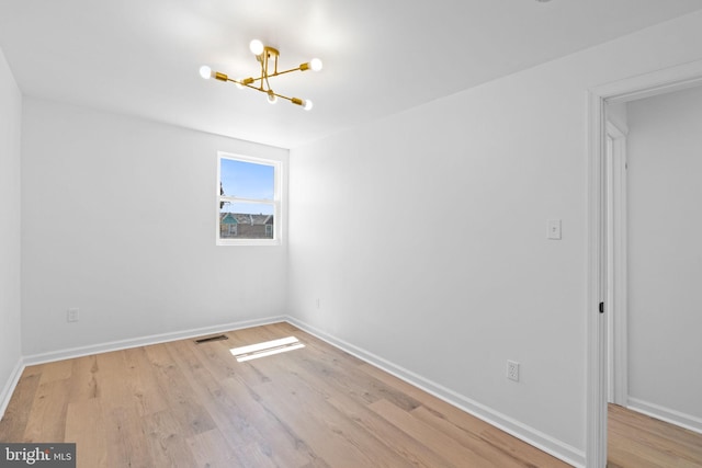 unfurnished room with a chandelier, wood finished floors, and baseboards