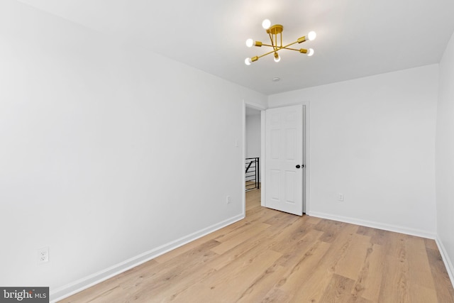 empty room featuring a chandelier, baseboards, and light wood-style flooring