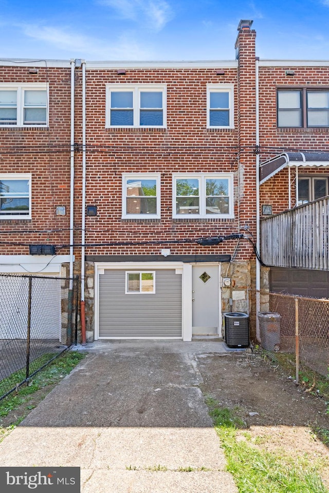back of property with concrete driveway, an attached garage, central AC, fence, and brick siding