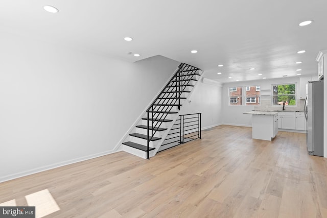 unfurnished living room with recessed lighting, light wood-style flooring, stairway, baseboards, and a sink