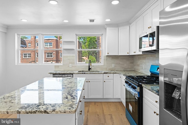 kitchen featuring appliances with stainless steel finishes, a sink, a center island, light wood-style floors, and white cabinetry