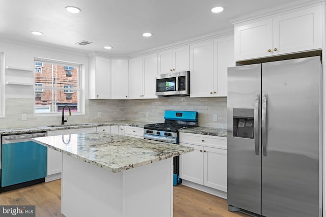 kitchen featuring appliances with stainless steel finishes, a sink, white cabinetry, a kitchen island, and light wood-style flooring