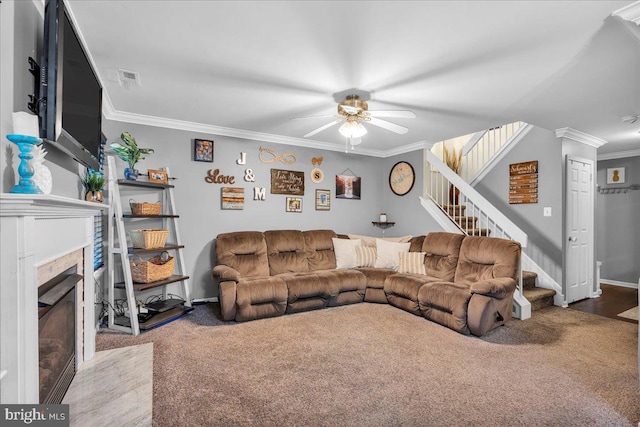living area with ornamental molding, stairs, a ceiling fan, carpet floors, and a fireplace with flush hearth
