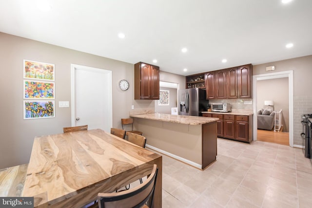kitchen with stainless steel refrigerator with ice dispenser, a peninsula, backsplash, light stone counters, and recessed lighting