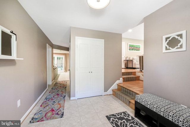 corridor featuring baseboards, light tile patterned floors, and stairs
