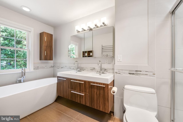 full bathroom with tile walls, toilet, a freestanding bath, double vanity, and a wainscoted wall