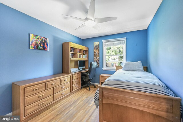 bedroom with light wood-style flooring, an office area, ceiling fan, and baseboards