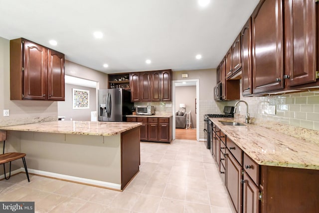 kitchen featuring stainless steel appliances, a sink, backsplash, a peninsula, and light stone countertops