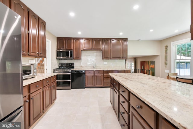 kitchen featuring appliances with stainless steel finishes, backsplash, light stone counters, recessed lighting, and a sink