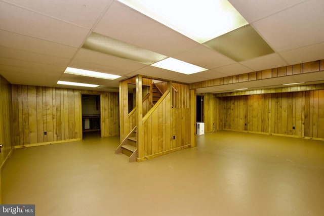 finished basement with a drop ceiling, stairway, and wooden walls