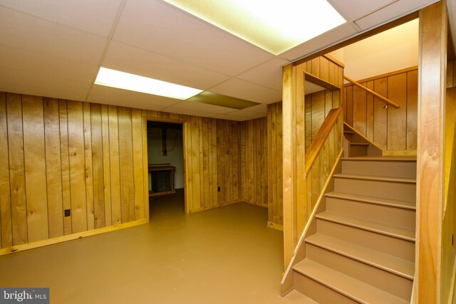 finished basement with a paneled ceiling, stairs, and wood walls