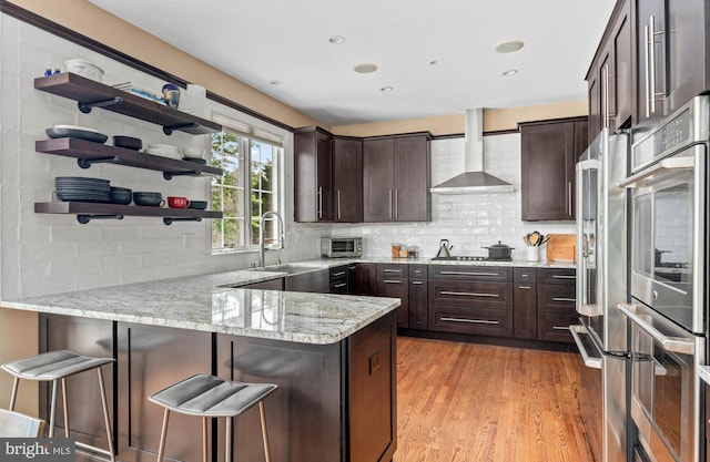 1123 Riverview Ln, Conshohocken, PA 19428 - kitchen with wall chimney exhaust hood, a peninsula, dark brown cabinets, open shelves, and light wood-type flooring