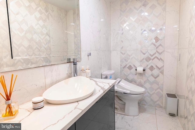 bathroom with tile walls, toilet, vanity, and marble finish flooring
