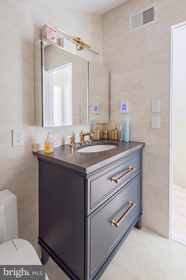 half bath with tile walls, vanity, toilet, and tile patterned floors