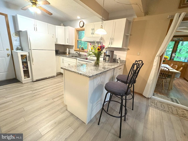 kitchen featuring white appliances, a peninsula, under cabinet range hood, light stone counters, and a sink