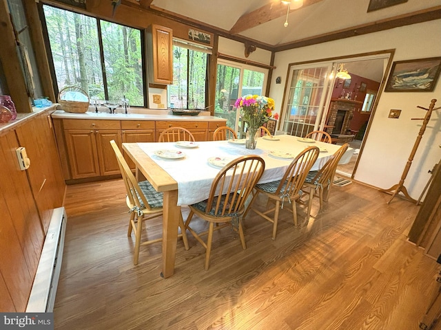 dining space featuring vaulted ceiling, light wood-type flooring, a brick fireplace, and baseboard heating