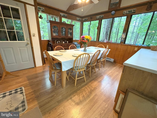 dining room with healthy amount of natural light, a ceiling fan, baseboard heating, light wood-type flooring, and wood walls