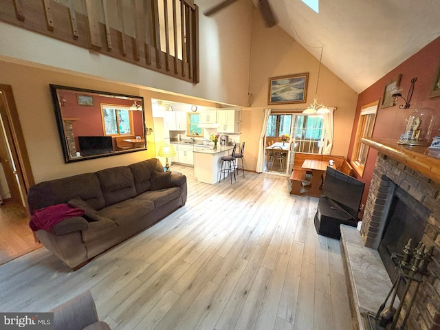 living room featuring high vaulted ceiling, a fireplace, and light wood-type flooring