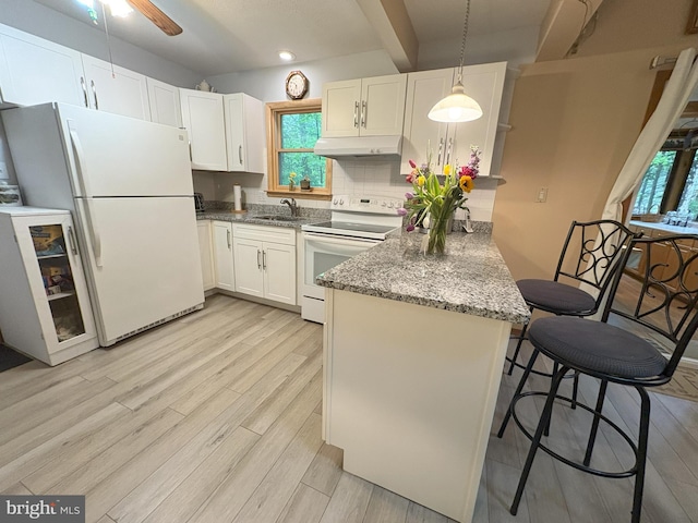kitchen with white appliances, under cabinet range hood, a peninsula, a sink, and white cabinetry