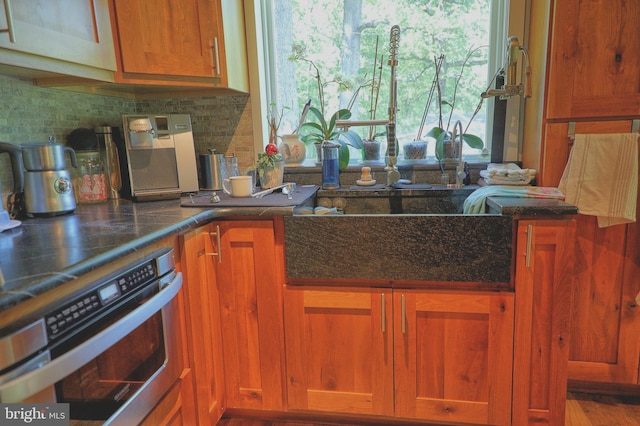 14308 Bristow Rd, Manassas, VA 20112 - kitchen featuring stainless steel oven, backsplash, brown cabinets, and dark stone countertops