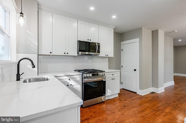 kitchen featuring appliances with stainless steel finishes, a sink, light wood-style flooring, white cabinets, and decorative backsplash