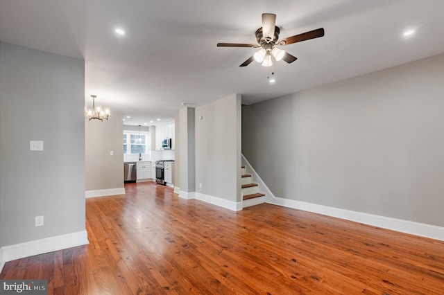 unfurnished living room with a ceiling fan, a chandelier, stairway, wood finished floors, and baseboards