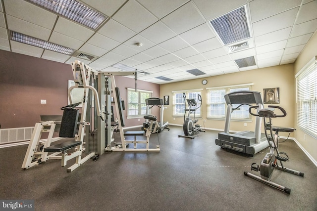 exercise room featuring a paneled ceiling and baseboards