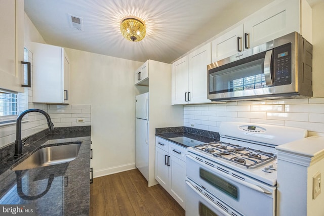 kitchen featuring white appliances, a sink, backsplash, dark stone counters, and dark wood-style flooring