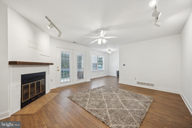 unfurnished living room featuring track lighting, a glass covered fireplace, ceiling fan, dark wood-type flooring, and baseboards