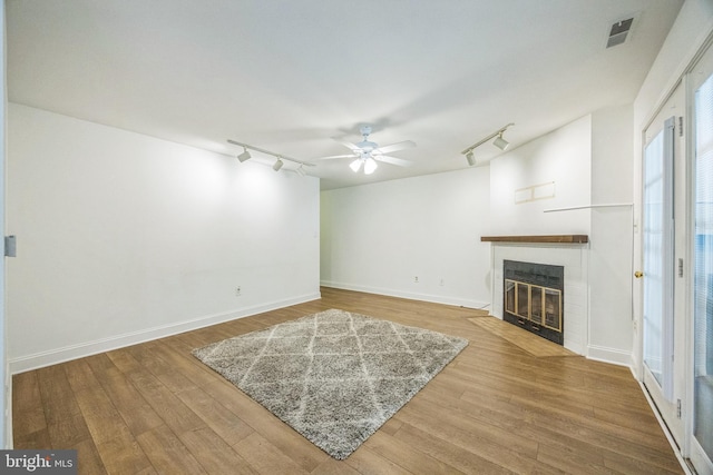 unfurnished living room with rail lighting, wood finished floors, a fireplace with flush hearth, and a ceiling fan
