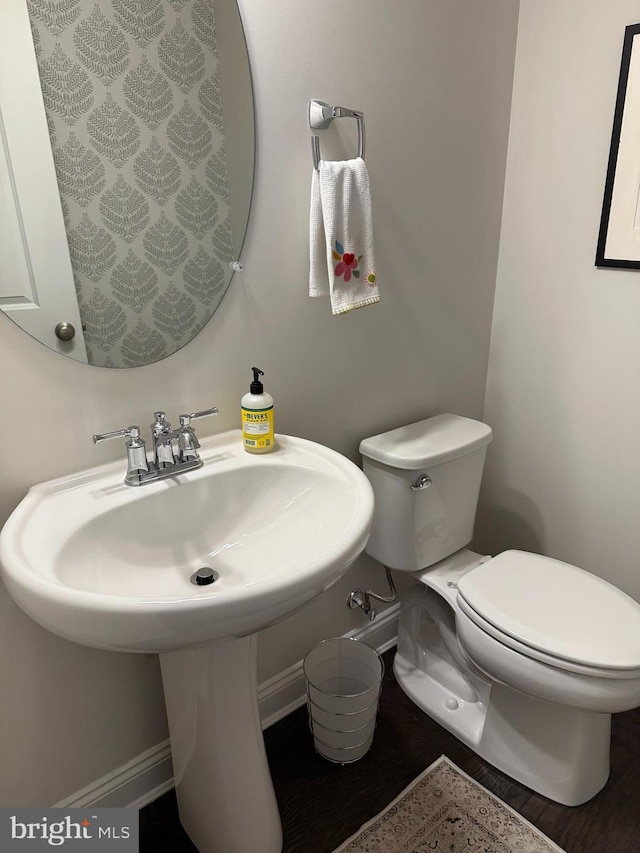 bathroom with toilet, baseboards, wood finished floors, and a sink