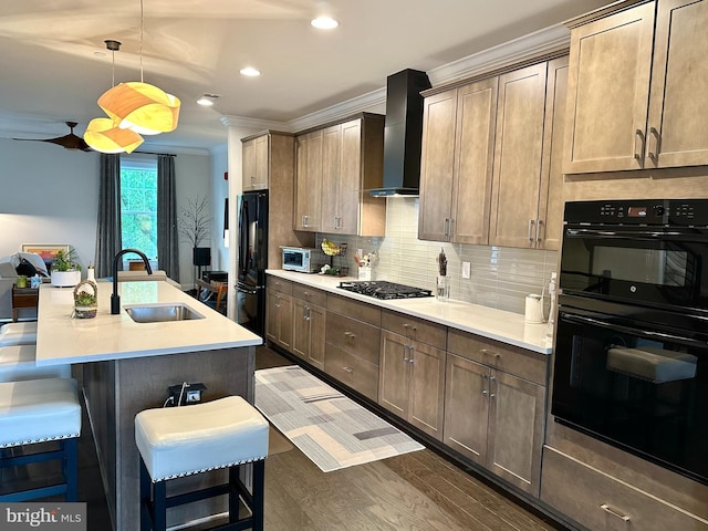kitchen featuring a sink, wall chimney range hood, black appliances, ornamental molding, and a kitchen bar