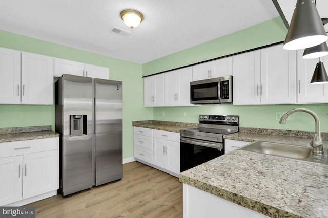 kitchen featuring appliances with stainless steel finishes, a sink, white cabinets, light wood-type flooring, and decorative light fixtures