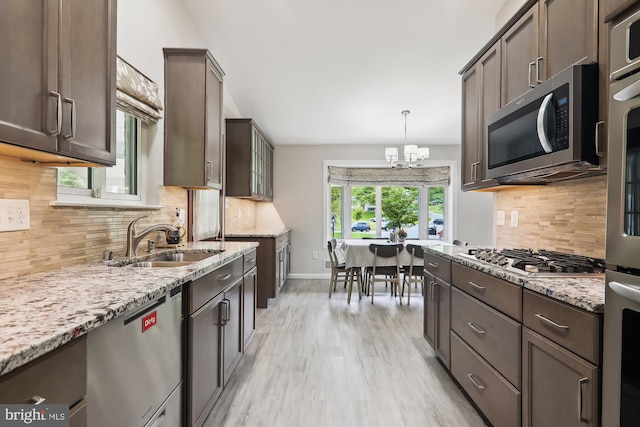 kitchen with appliances with stainless steel finishes, a sink, light wood-style flooring, light stone counters, and backsplash