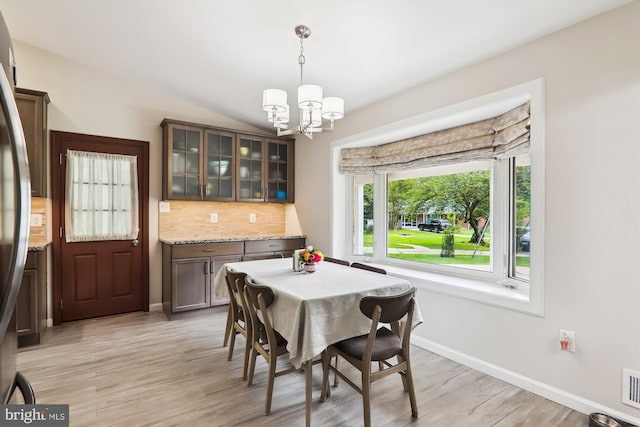 dining space featuring a chandelier, light wood-style flooring, baseboards, and vaulted ceiling