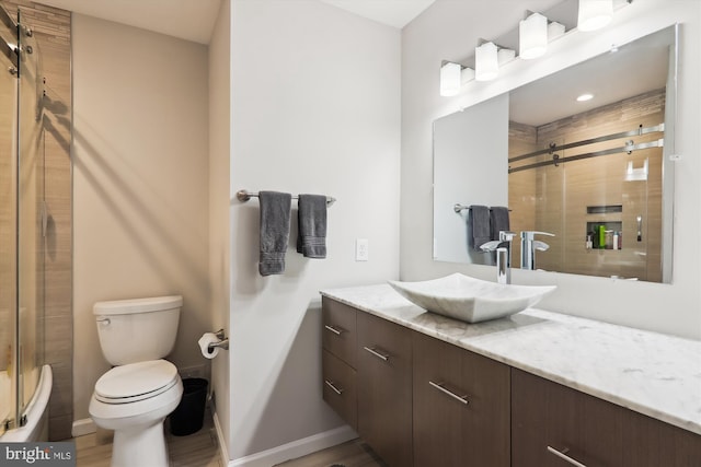 bathroom featuring baseboards, toilet, a shower with shower door, vanity, and wood finished floors