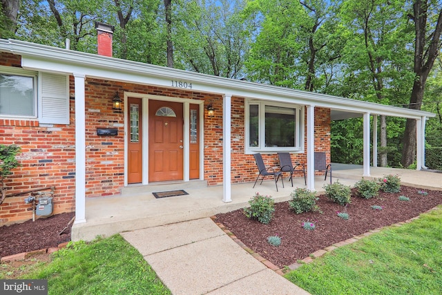 doorway to property with covered porch, brick siding, and a chimney