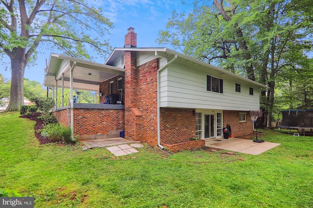 rear view of property with a trampoline, a chimney, a yard, brick siding, and a patio