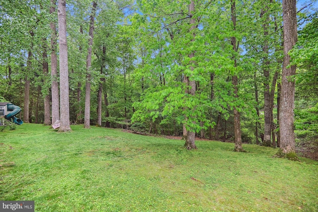 view of green lawn featuring a wooded view