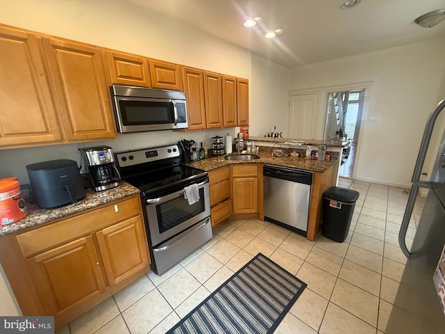 kitchen featuring appliances with stainless steel finishes, a peninsula, light tile patterned flooring, dark stone counters, and recessed lighting