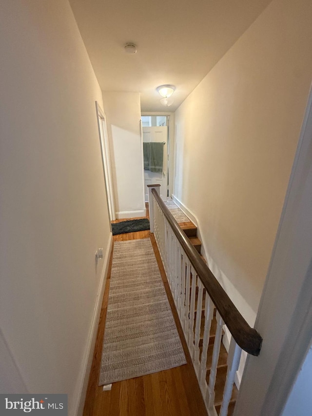 hall featuring an upstairs landing, baseboards, and wood finished floors