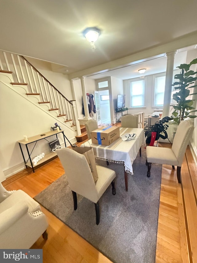 dining space with decorative columns, wood finished floors, and stairs