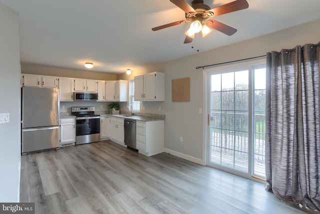 kitchen with appliances with stainless steel finishes, white cabinetry, light wood-type flooring, and a ceiling fan