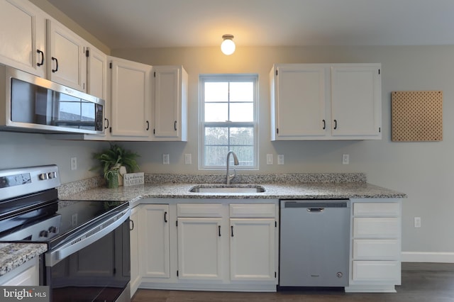 kitchen featuring appliances with stainless steel finishes, a sink, white cabinets, and light stone countertops