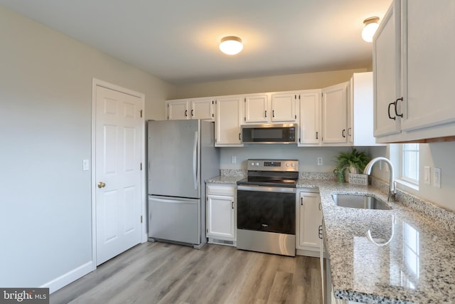kitchen featuring stainless steel appliances, a sink, light stone counters, and light wood-style flooring