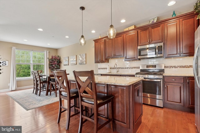 kitchen with appliances with stainless steel finishes, light wood-style flooring, a center island, backsplash, and recessed lighting