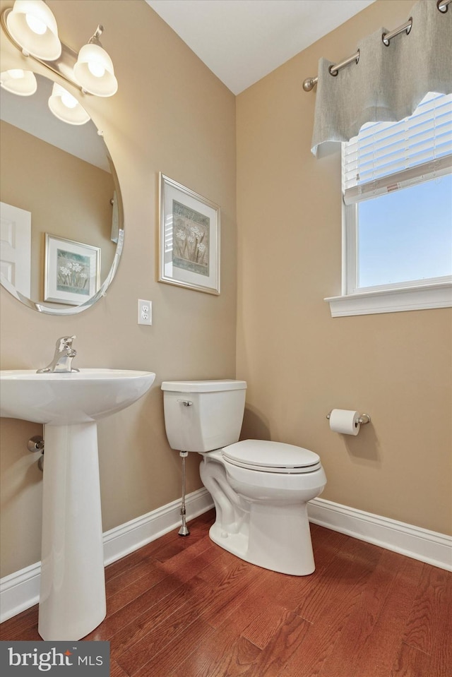bathroom featuring baseboards, wood finished floors, toilet, and a sink