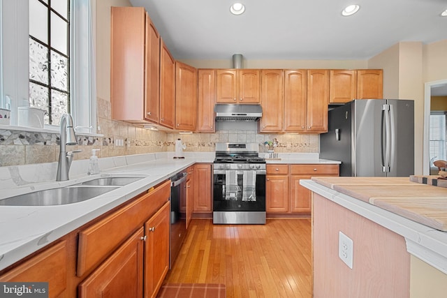 6051 Piney Grove Way, Gainesville, VA 20155 - kitchen with stainless steel appliances, under cabinet range hood, a sink, light wood-style flooring, and decorative backsplash
