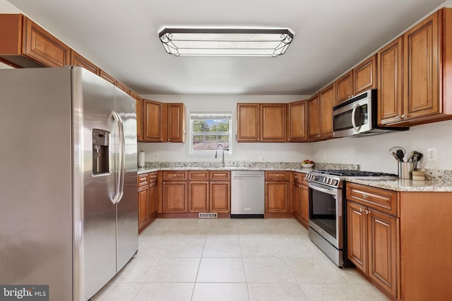6311 Gentele Ct, Alexandria, VA 22310 - kitchen featuring appliances with stainless steel finishes, brown cabinetry, light stone counters, light tile patterned flooring, and a sink